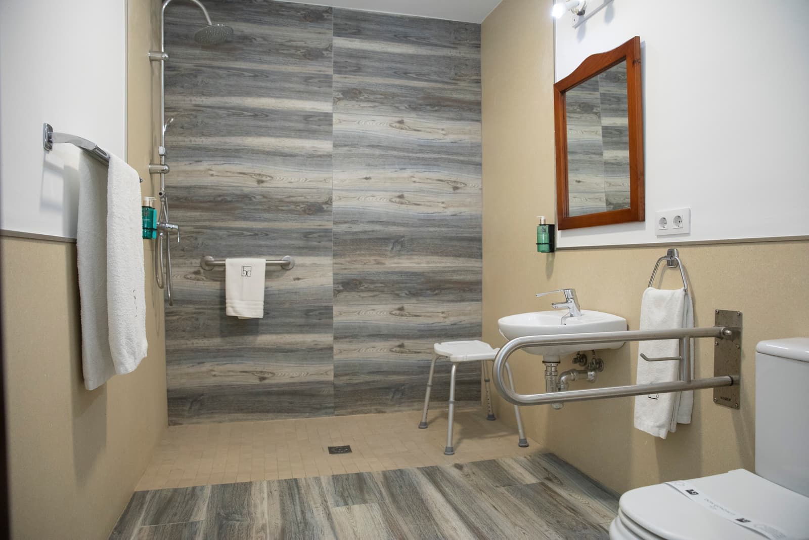 Baño adaptado con ducha a ras de suelo, asideros en la pared, silla de ducha abatible y lavabo con espacio libre debajo