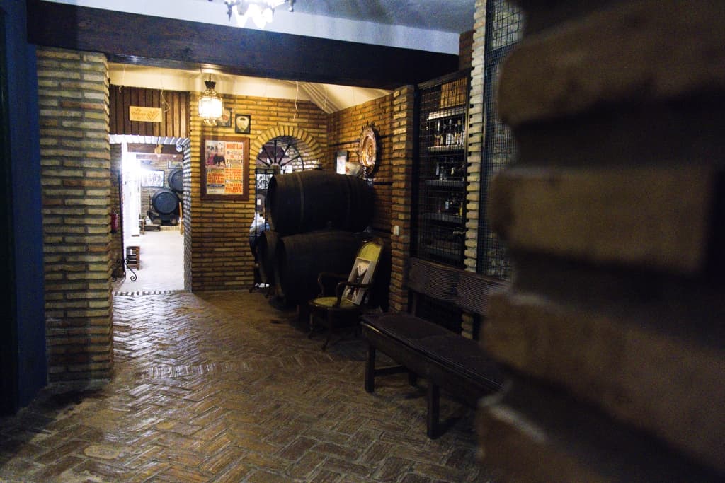 Bodega con paredes de ladrillo visto, barricas de vino, botellero y suelo de baldosa en espiga