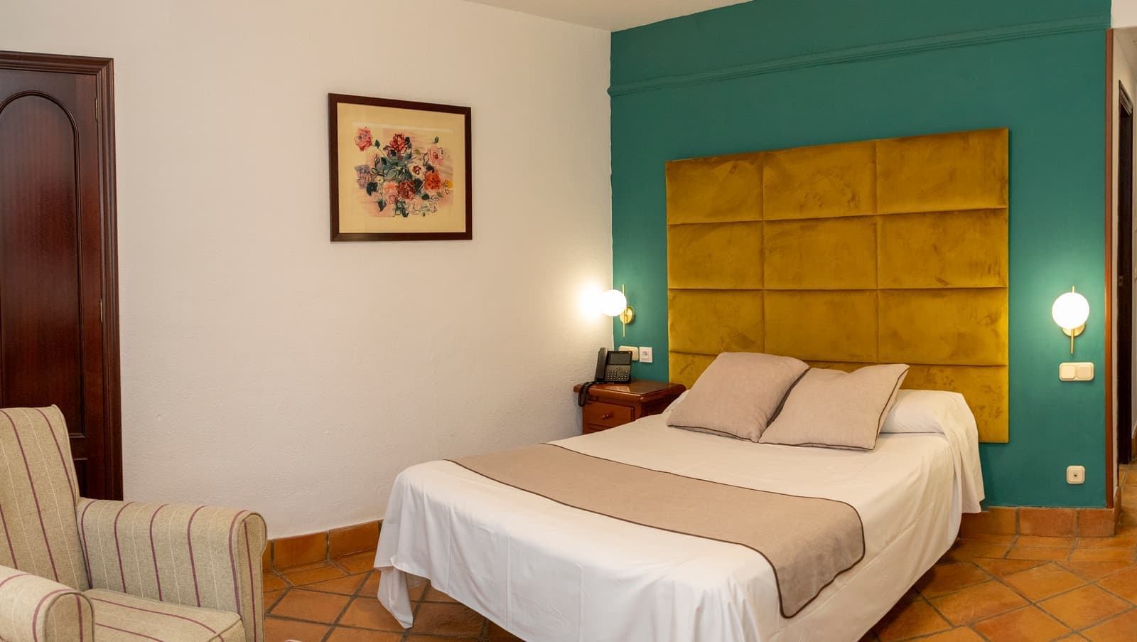 Vista panorámica de una habitación con pared verde, cabecero amarillo, cama de matrimonio y butaca