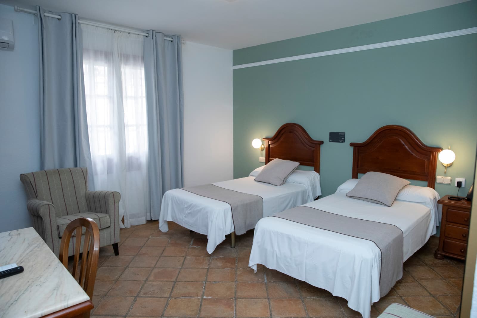 Habitación con dos camas individuales, dos butacas tapizadas y pared en verde agua