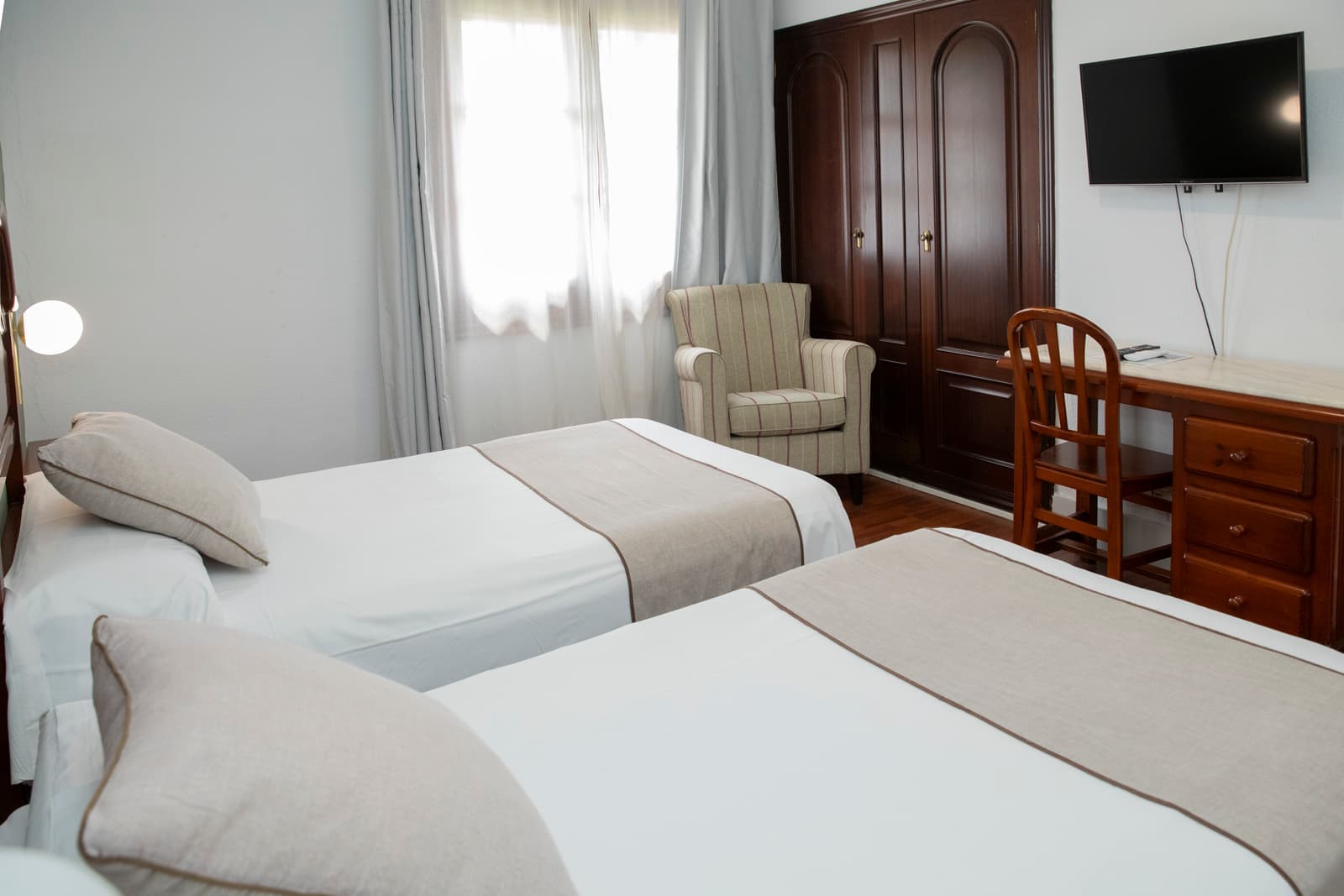 Habitación con dos camas, escritorio, armario de madera y televisión