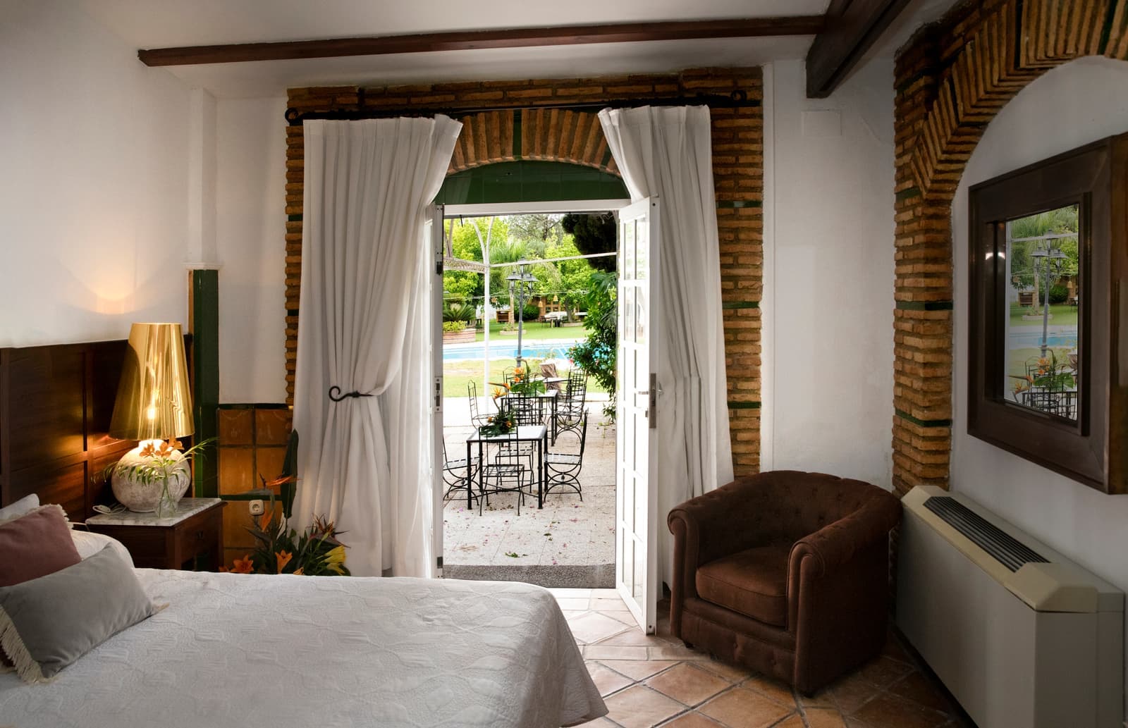 Habitación con puerta acristalada abierta a una terraza con mesa y sillas, butaca de piel y techo con vigas