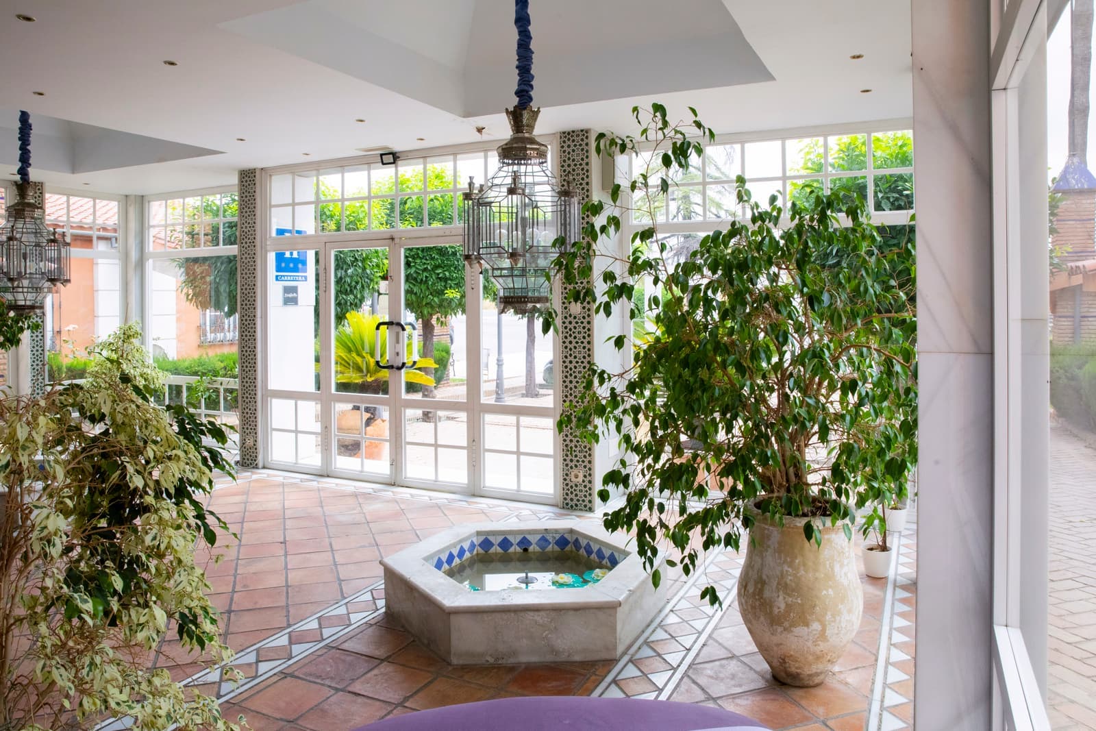 Patio acristalado con fuente octogonal de azulejos y plantas de gran porte