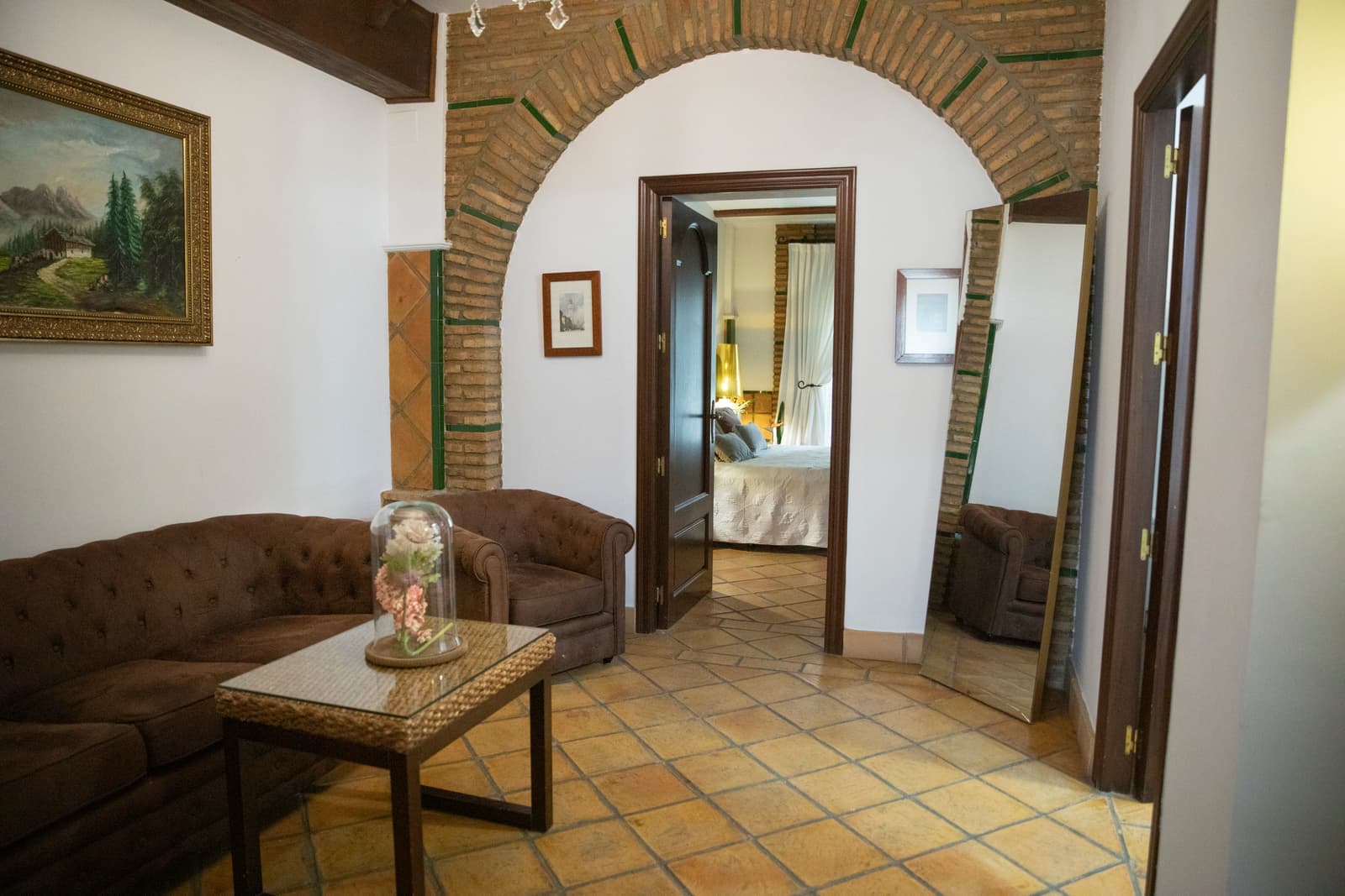 Salón con sofá chéster de piel, mesa baja y arco de ladrillo visto que da paso al dormitorio